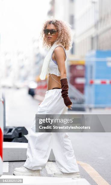 Influencer Michele Winchester, wearing white pants by Emmiol, a white shirt with a wide scarf by Emmiol, brown arm cuffs by Emmiol, white shoes by...