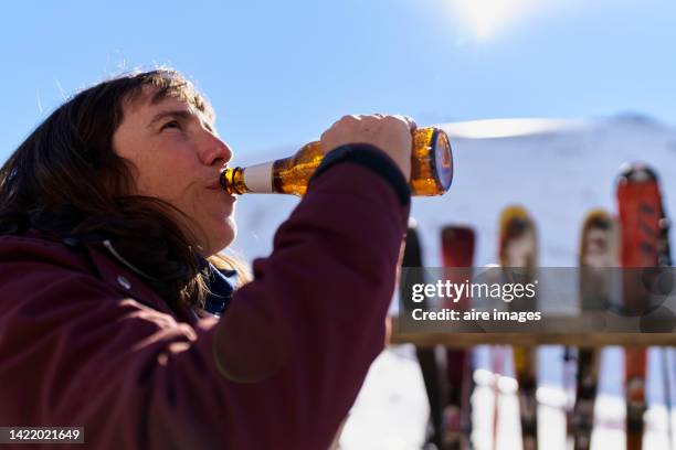 woman drinking a beer outdoors after finishing skiing on a sunny winter day, in the background out of focus image of skis lying on wooden fence. - mountains alcohol snow bildbanksfoton och bilder