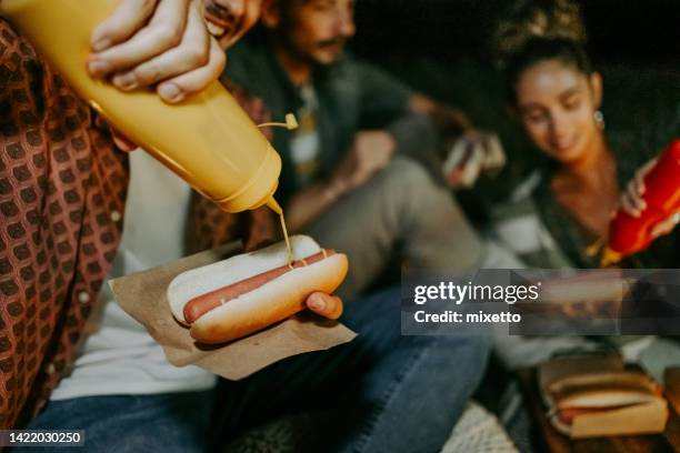friends enjoying hot dogs while camping outdoors - hotdog stockfoto's en -beelden