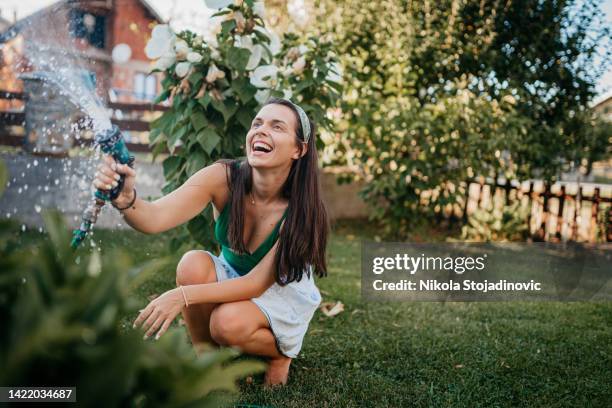 a woman sprays a hose in the yard - garden hose stock pictures, royalty-free photos & images
