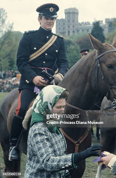 As an unidentified rider and horse stand behind her, Queen Elizabeth II is handed an award ribbon at the Royal Windsor Horse Show, Windsor, England,...