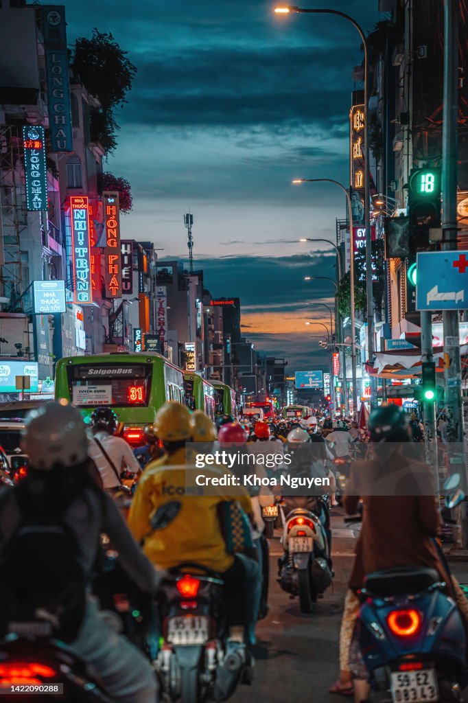 Rush hour, busy traffic jam during sunset and colorful perspective of Hai Ba Trung St with numerous hotel, bar and shop sign boards, crowded with people, motorbikes