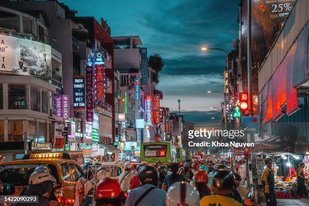 rush hour, busy traffic jam during sunset and colorful perspective of hai ba trung st with numerous hotel, bar and shop sign boards, crowded with people, motorbikes - hochi minh stock pictures, royalty-free photos & images