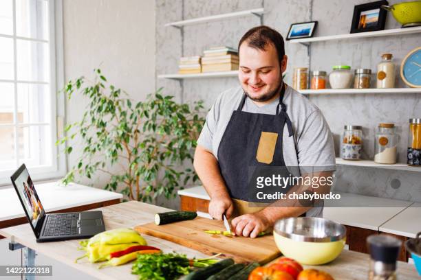 happy man cooking healthy meal in kitchen - fat man stock pictures, royalty-free photos & images