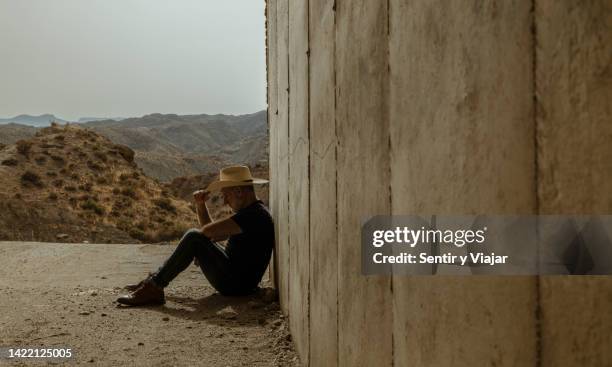 Portrait of adult man in cowboy hat sitting on ground in entrance of tunnel