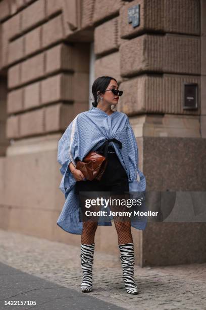 Farah Assaad is seen wearing black shades, silver large earrings, white/blue checked oversize shirt, black Alexander Wang shorts, black fishnet...