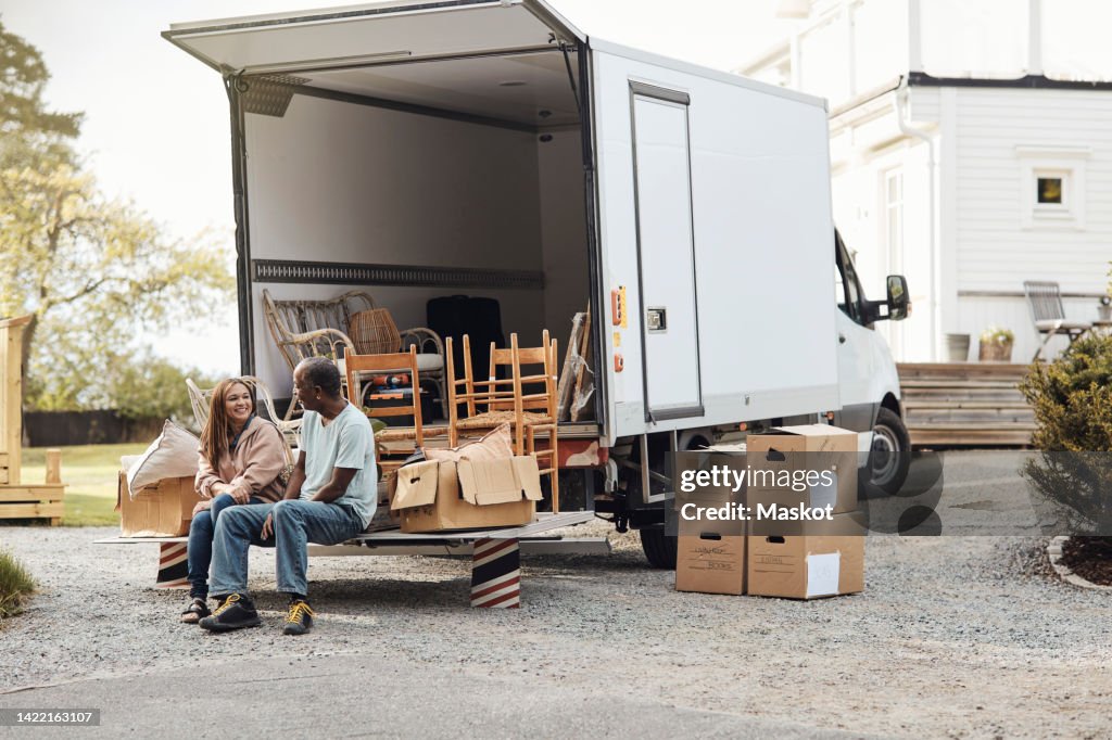 Couple talking to each other while sitting by cardboard boxes near van