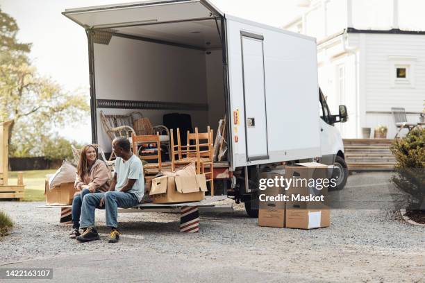 couple talking to each other while sitting by cardboard boxes near van - verhuiswagen stockfoto's en -beelden