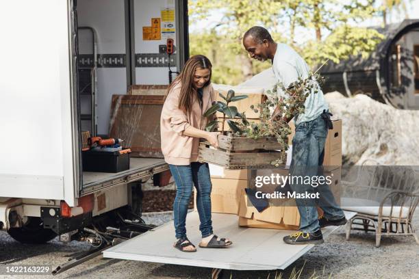 mature couple helping each other while unloading planter box from van - removal crates stock pictures, royalty-free photos & images