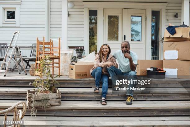 portrait of mature couple sitting on steps outside house - man with moving boxes authentic stockfoto's en -beelden