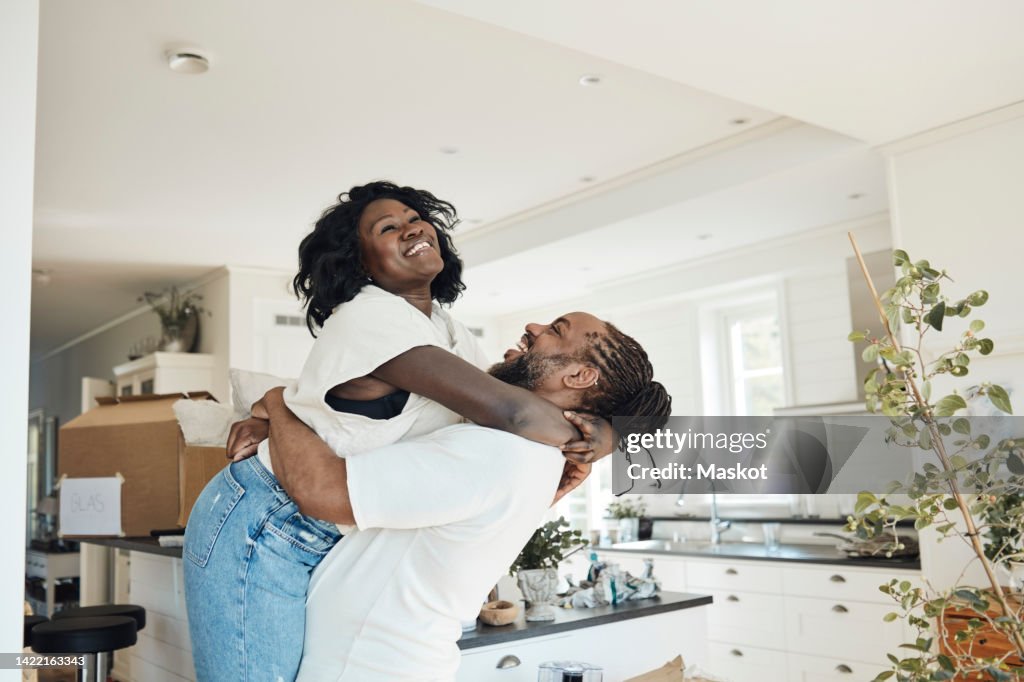 Side view of happy boyfriend lifting girlfriend while standing at home