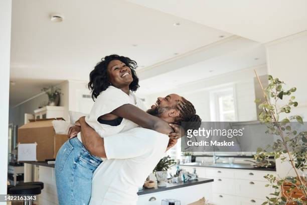 side view of happy boyfriend lifting girlfriend while standing at home - first girlfriend stock pictures, royalty-free photos & images