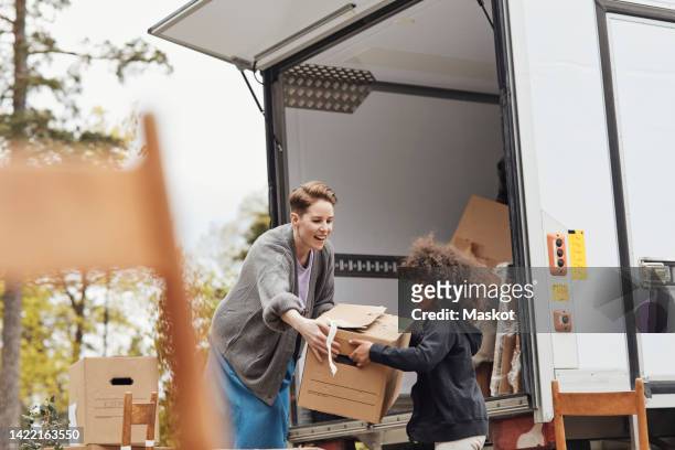 side view of boy helping mother in unloading cardboard box from van - déménagement photos et images de collection