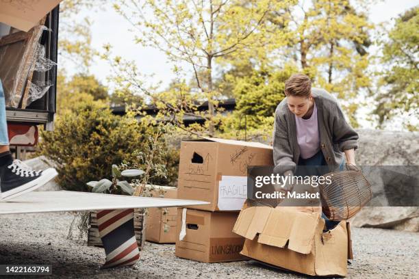 lesbian woman removing pillow and basket from cardboard box - moving truck stock pictures, royalty-free photos & images