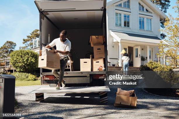 full length of man unloading cardboard box from van - körperliche aktivität stock-fotos und bilder