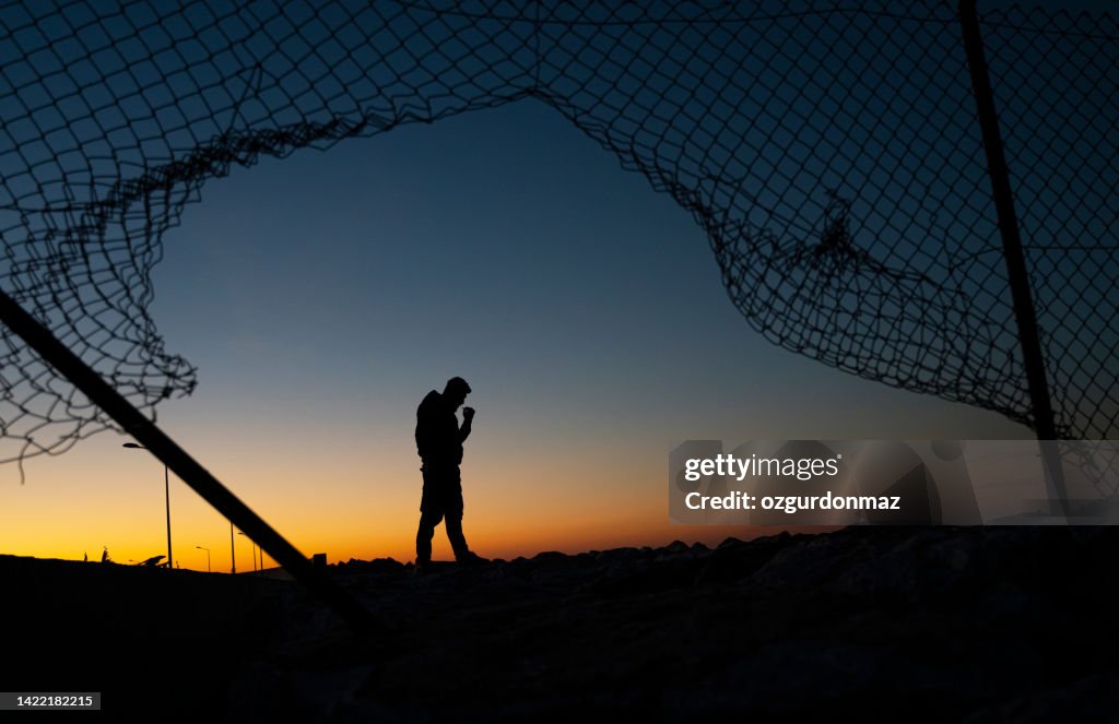 Refugee man standing behind the fence at sunrise
