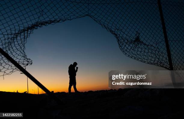 refugee man standing behind the fence at sunrise - evacuatiekamp stockfoto's en -beelden