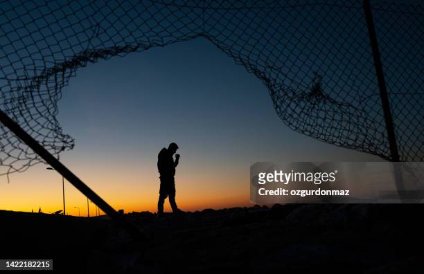 refugee man standing behind the fence at sunrise - prison fence stock pictures, royalty-free photos & images