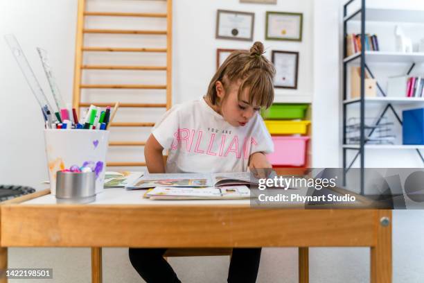 little girl with down syndrome reads a book - girl looking down stock pictures, royalty-free photos & images