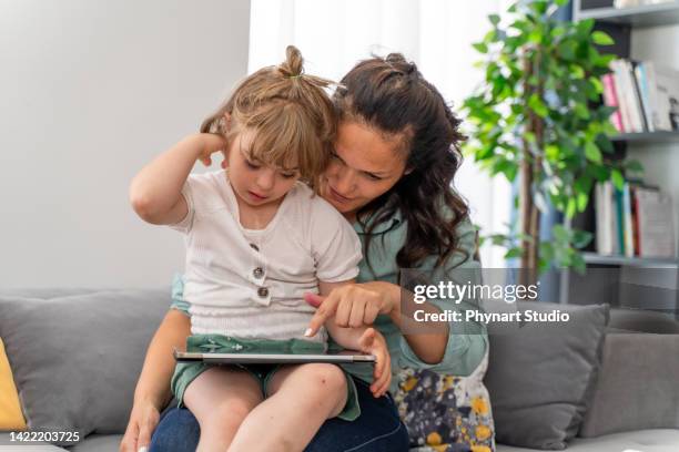 mãe madura e filha com síndrome de down em casa usando tablet digital - autism - fotografias e filmes do acervo