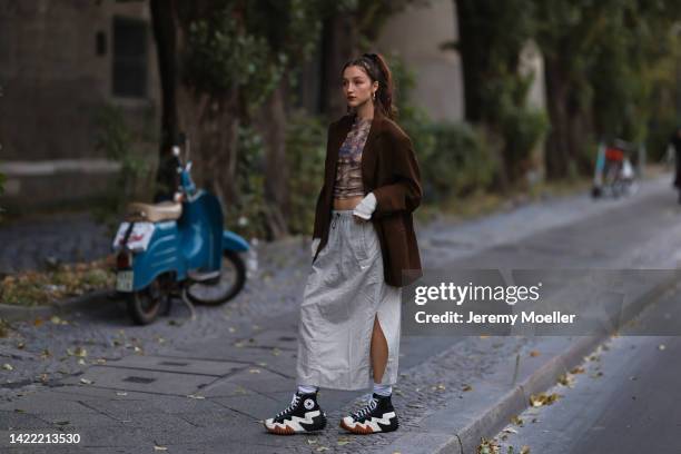 Caro Schaeffler is seen wearing colorful top, gold earrings, brown oversize blazer, beige cargo long skirt, beige knit gloves, white socks and black...