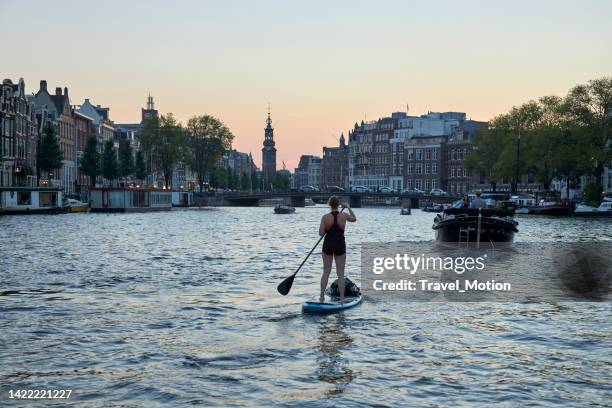 woman paddleboarding with the mint tower in the background at twilight, amsterdam - sup stockfoto's en -beelden