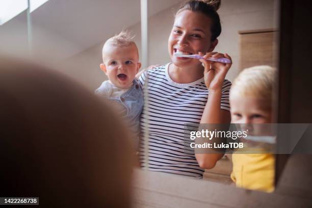 während die mutter den kleinen jungen in den armen hält, putzen sie und ihr anderer sohn sich die zähne - baby tooth stock-fotos und bilder