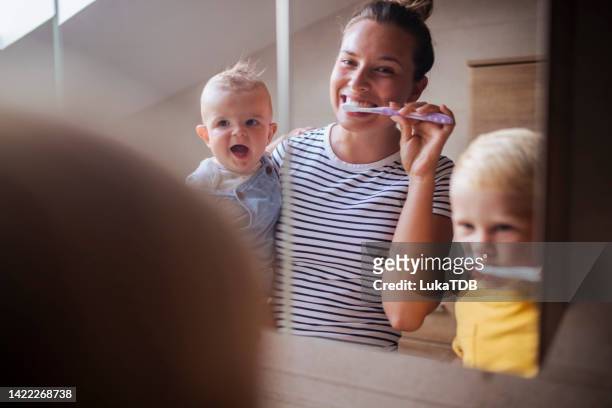 mientras la madre sostiene al bebé en sus brazos, ella y su otro hijo se cepillan los dientes. - angelica hale fotografías e imágenes de stock