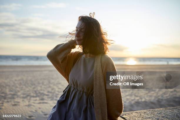 woman with tousled hair and closed eyes on the beach at sunset - warrig haar stockfoto's en -beelden