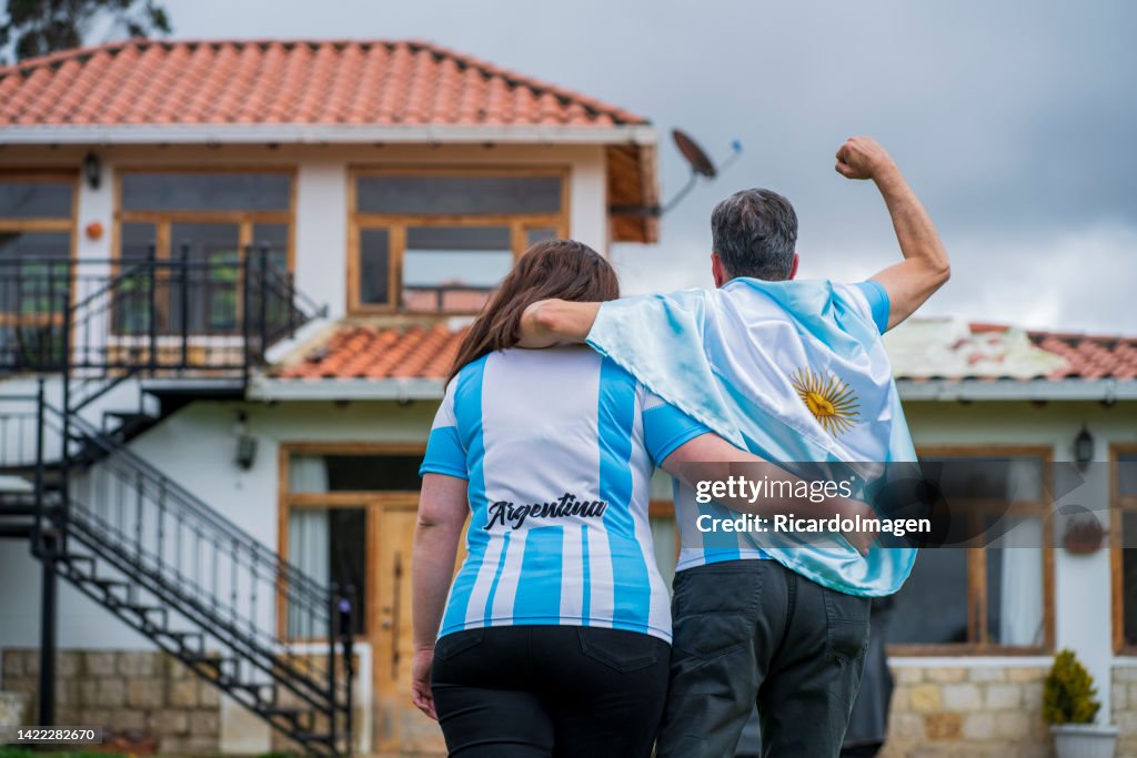 Two fans of the Argentine soccer team are together on the grass of their field celebrating a great goal