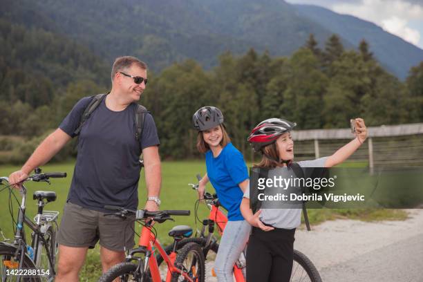 niña sonriente tomándose selfie con la familia cuando anda en bicicleta - hacer foto fotografías e imágenes de stock