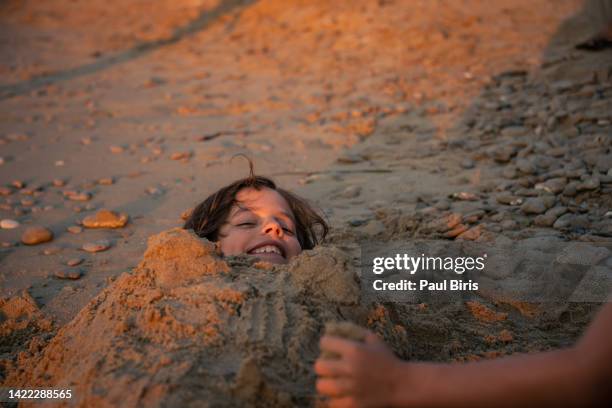 boy laughing while his brother buries him in the sand, zakynthos,  ionian islands, greece - buried alive stockfoto's en -beelden