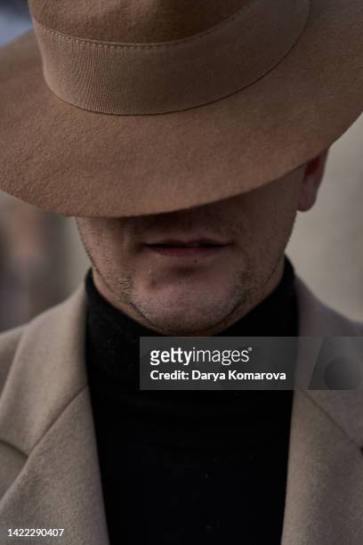 а handsome man in a beige hat and coat and a black turtleneck. historical reconstruction of a man of the 30s or 40s in a parisian park on a walk. retro fashion look on beige background. unrecognisable man in hat as a design element for a book cover. - costume beige stock pictures, royalty-free photos & images