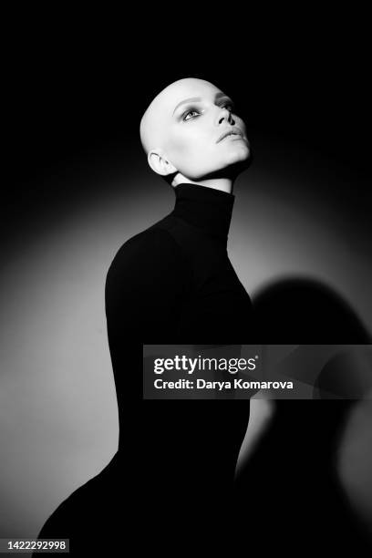 young woman with alopecia on black background with circle of light. bald woman with eyes make up and black turtleneck. black and white portrait of beautiful lady without hair and with no lashers and brows. - calvizie foto e immagini stock