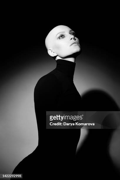 young woman with alopecia on black background with circle of light. bald woman with eyes make up and black turtleneck. black and white portrait of beautiful lady without hair and with no lashers and brows. - strong hair 個照片及圖片檔