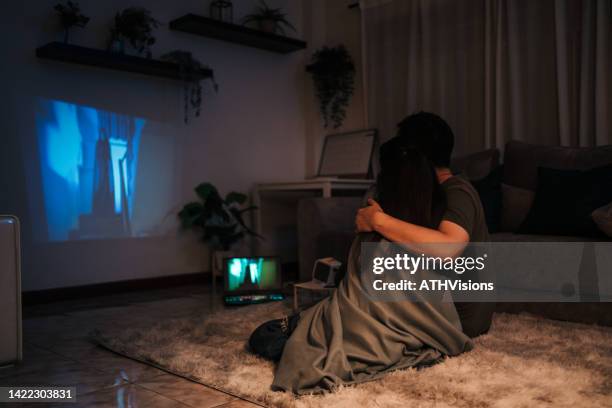 pareja sentada en el suelo viendo un thriller en el projector tv por la noche - horror movie fotografías e imágenes de stock