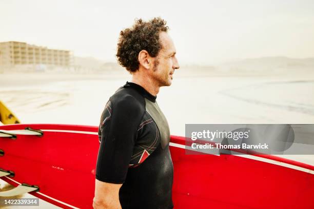 medium shot of man at waters edge watching surf before surf session - alleen oudere mannen stockfoto's en -beelden