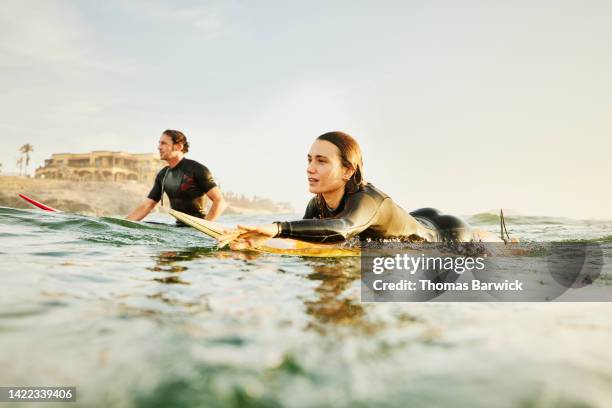 medium wide shot of female surfer paddling into lineup while surfing - selective focus imagens e fotografias de stock