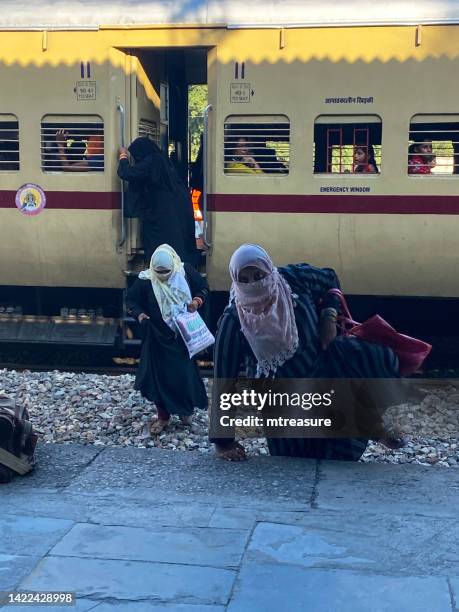 close-up image of passengers descending from second class train carriage, passengers walking across rail track gravel to climb up on platform of bijnor railway station, india - overloaded passenger trains in india stock pictures, royalty-free photos & images