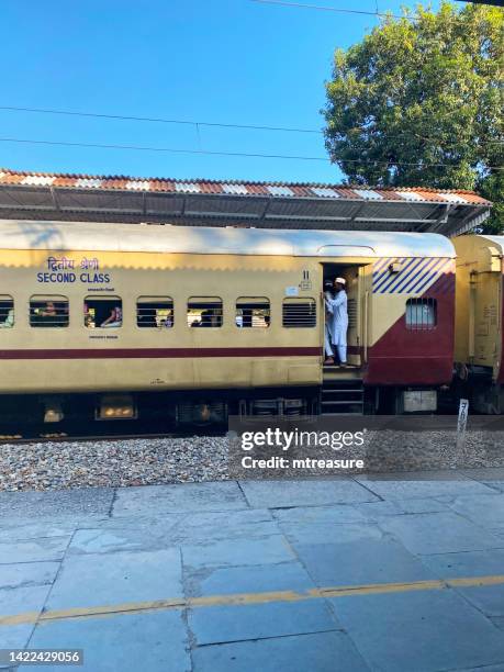 image of second class train carriage, passenger hanging out open door of a train on rail track of bijnor railway station, india - overloaded passenger trains in india stock pictures, royalty-free photos & images