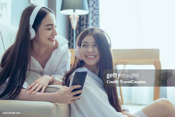 happy two lesbian woman. lgbtq homosexual lesbian couples sharing earphones while listening music over smart phone in living room. gay woman couple rest and relaxing by using smartphone in bedroom. - asian lesbians kiss stock pictures, royalty-free photos & images