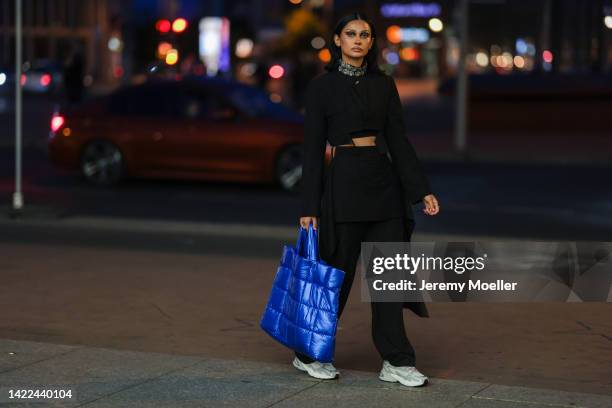 Wana Limar is seen wearing a large diamond necklace, black cropped sweater, black cargo pants, blue shopper bag and white Adidas sneaker, before...