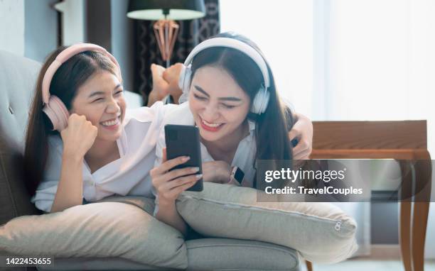 happy two lesbian woman. lgbtq homosexual lesbian couples sharing earphones while listening music over smart phone in living room. gay woman couple rest and relaxing by using smartphone in bedroom. - asian lesbians kiss stock pictures, royalty-free photos & images