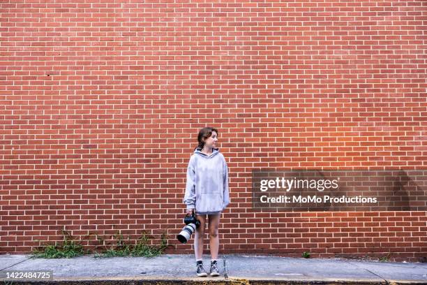 young woman holding dslr camera in urban neighborhood - young photographer stock pictures, royalty-free photos & images