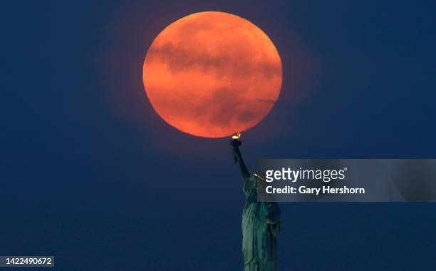 The full Harvest Moon sets behind the Statue of Liberty as the sun rises on September 10 in New York City.