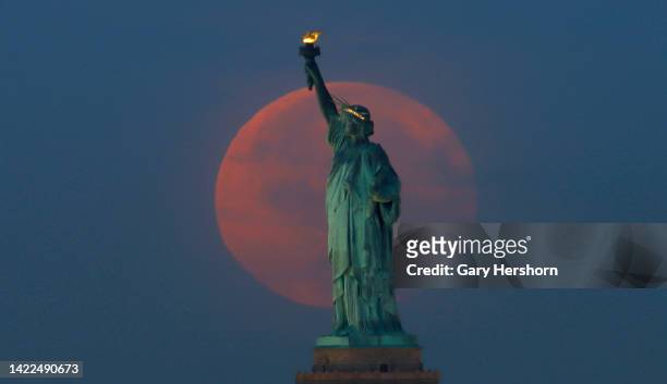 The full Harvest Moon sets behind the Statue of Liberty as the sun rises on September 10 in New York City.