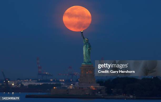 The full Harvest Moon sets behind the Statue of Liberty as the sun rises on September 10 in New York City.