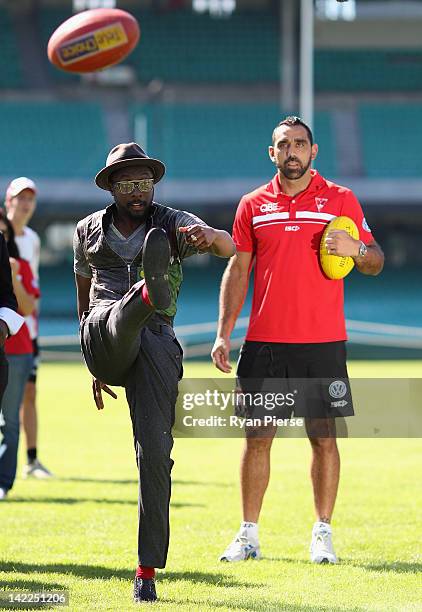 Will.i.am from The Black Eyed Peas kicks and AFL football as Adam Goodes from the Sydney Swans looks on during a young indigenous AFL players clinic...