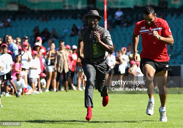 Will.i.am from The Black Eyed Peas runs against Adam Goodes from the Sydney Swans during a young indigenous AFL players clinic at Sydney Cricket...