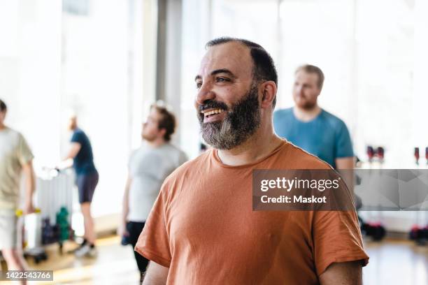 smiling man looking away with male friends in background at exercise class - nahöstlicher abstammung stock-fotos und bilder